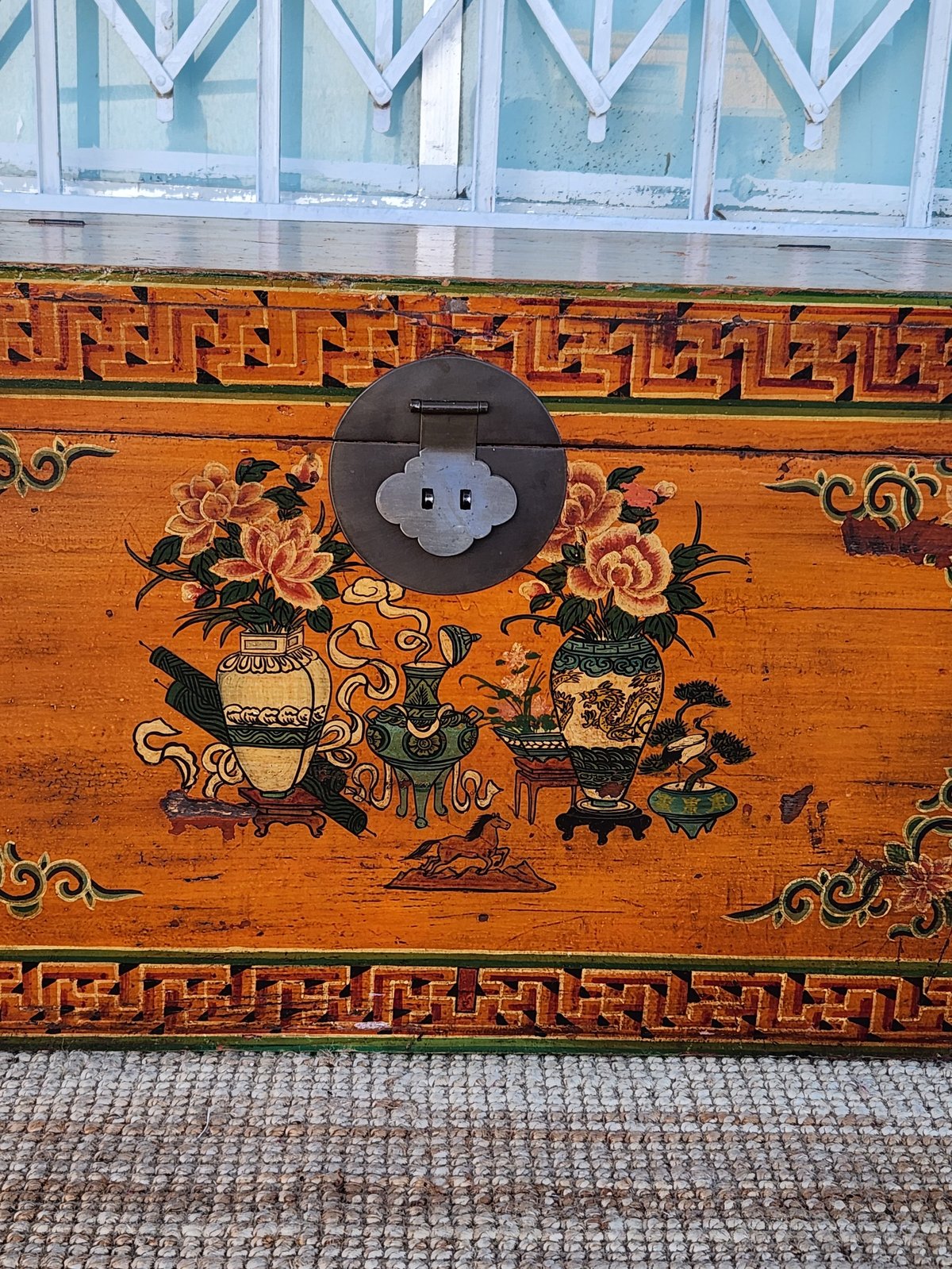 Ornate wooden chest with decorative Asian artwork and geometric patterns, featuring a black metal handle on top