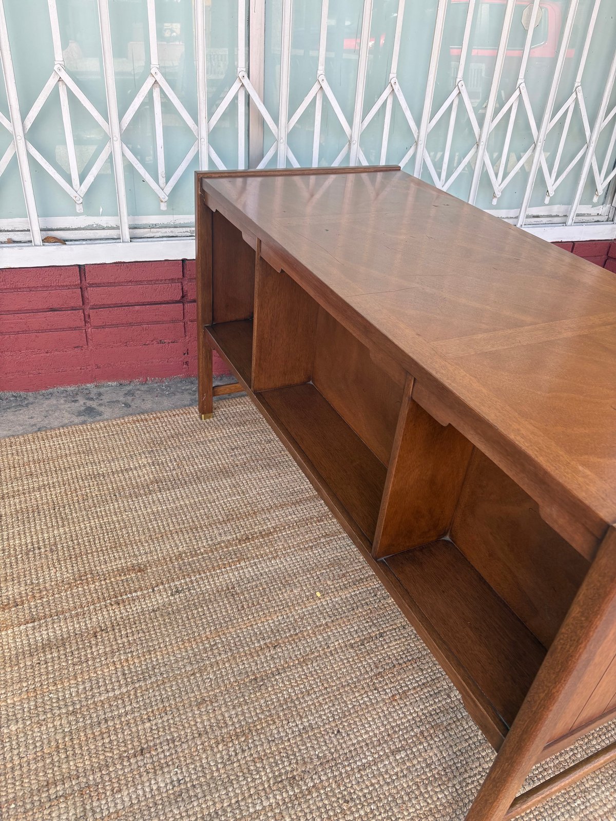 Wooden desk with open storage shelves in front of a white lattice gate and red brick wall