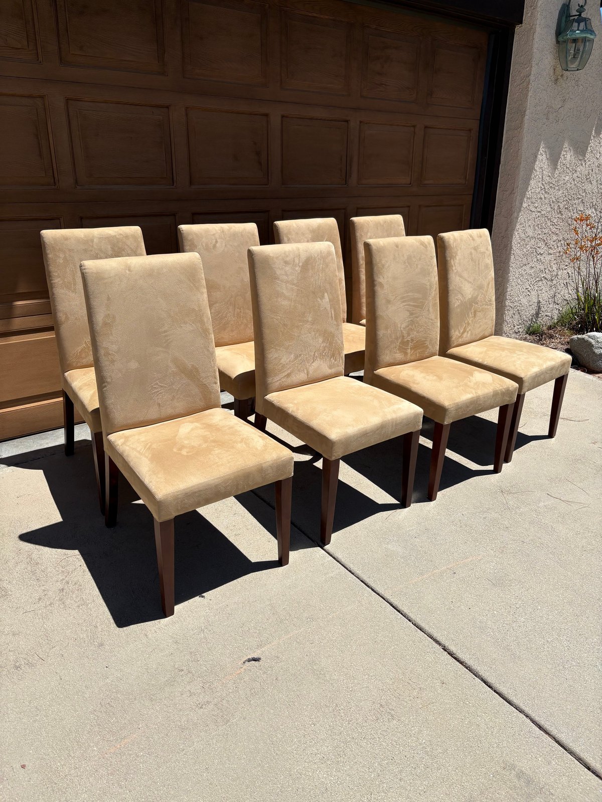 Set of six beige upholstered dining chairs with wooden legs arranged on a driveway in front of a garage door