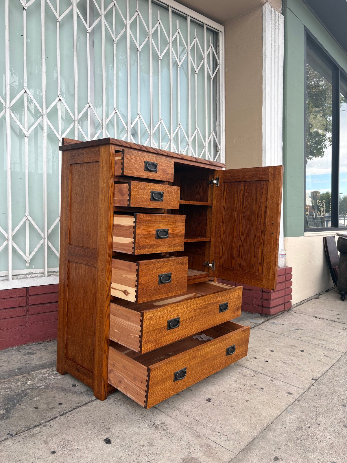 Wooden dresser with multiple drawers displayed outdoors on a concrete patio next to a decorative metal gate