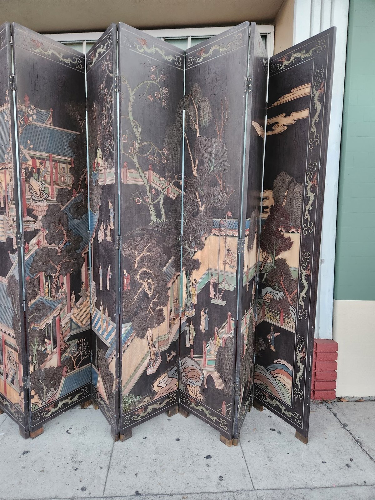 Antique Asian folding room divider screen with dark panels featuring gold leaf artwork and traditional landscape scenes