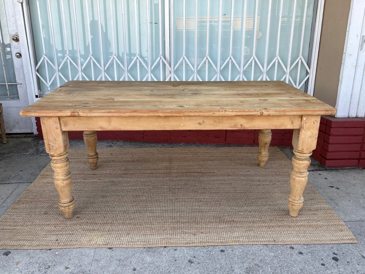 Wooden dining table with turned legs on a rug, set in front of white vertical blinds and closed white door