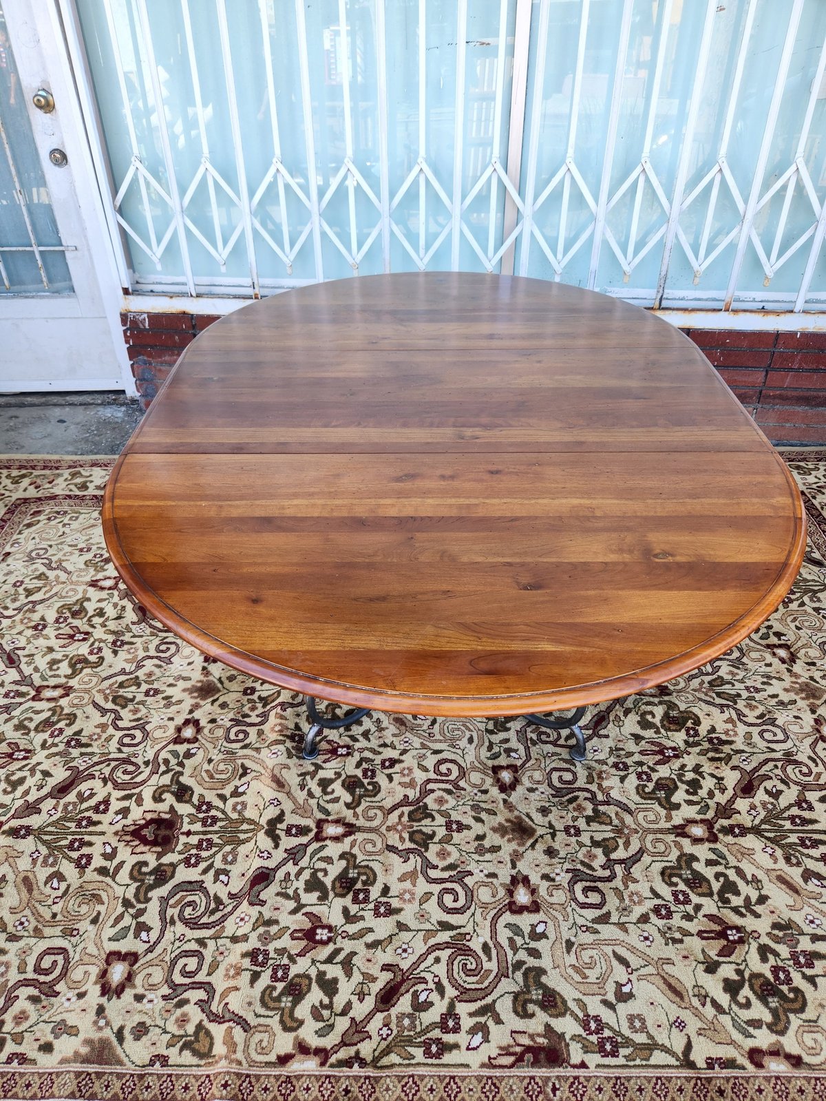 Wooden oval dining table with curved edges on patterned rug, white accordion door and windows in background