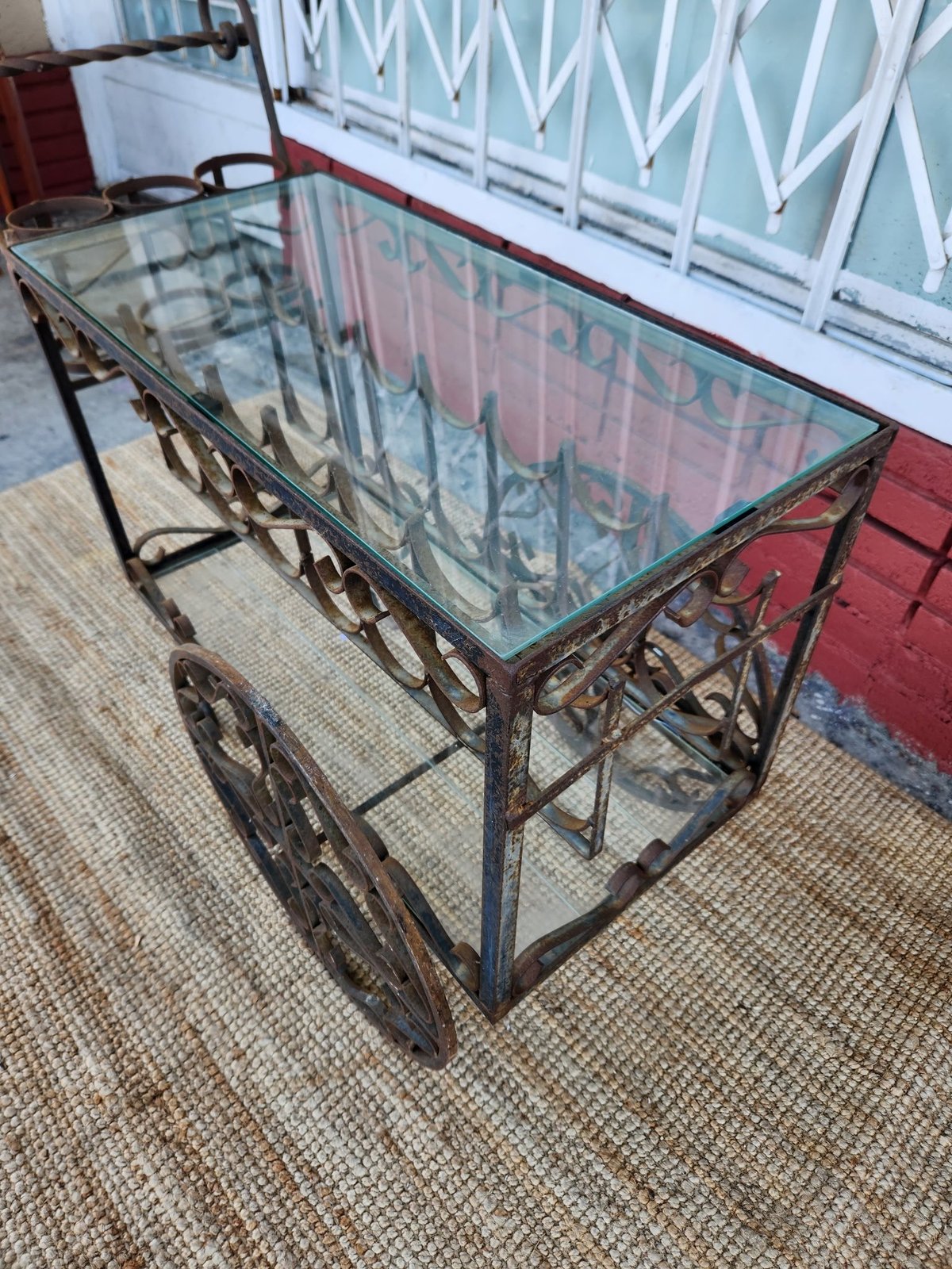 Vintage metal cart with glass top and large wheels displayed indoors on beige carpeting