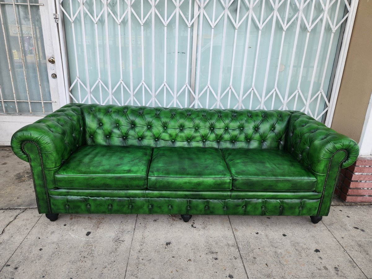 Green leather Chesterfield sofa with rolled arms and tufted back sitting on a sidewalk
