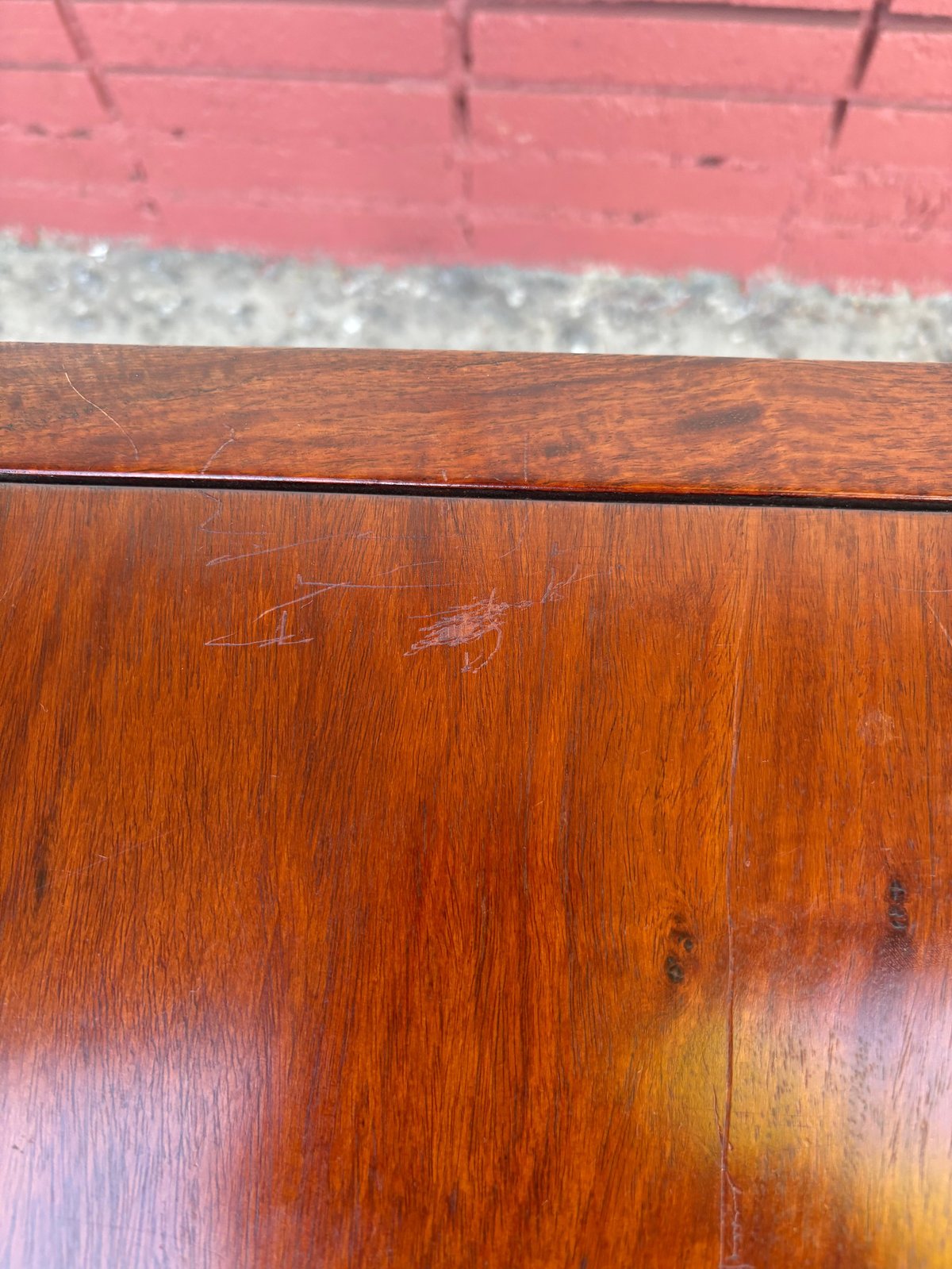 Close-up of wooden surface with visible scratches and wear marks, red wall in background