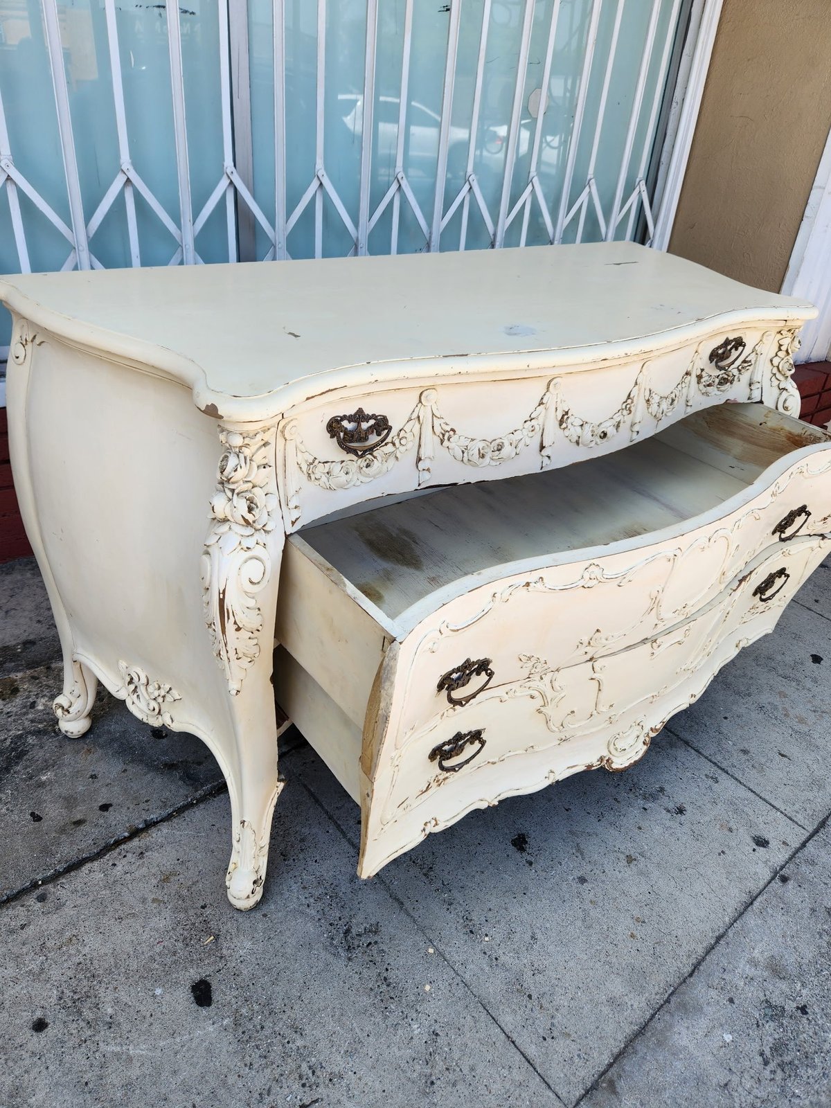 Vintage cream-colored nightstand with ornate curved legs and two drawers, showing distressed chippy paint finish