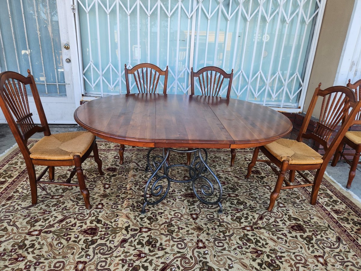 Oval wooden dining table with four wheeled metal legs and six matching wooden chairs with cream cushions on patterned rug