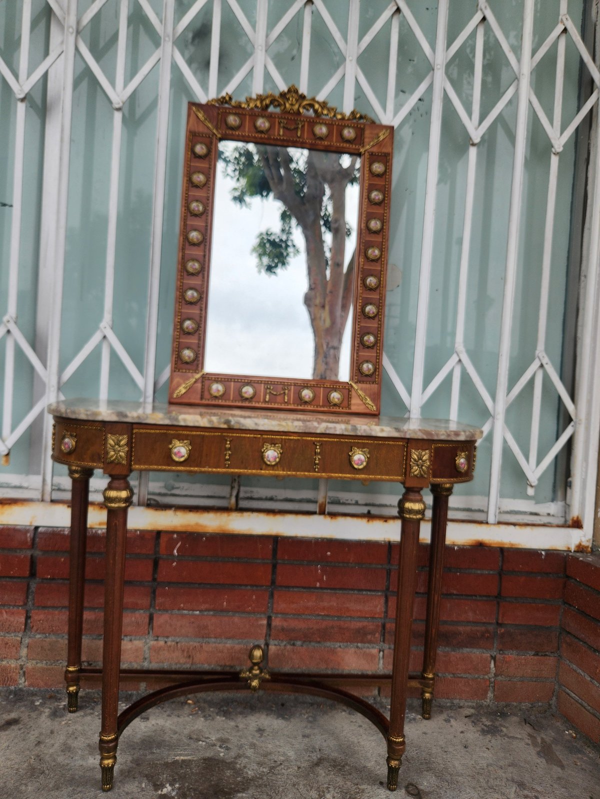 Antique wooden vanity with ornate mirror and brass hardware against striped wall and brick base