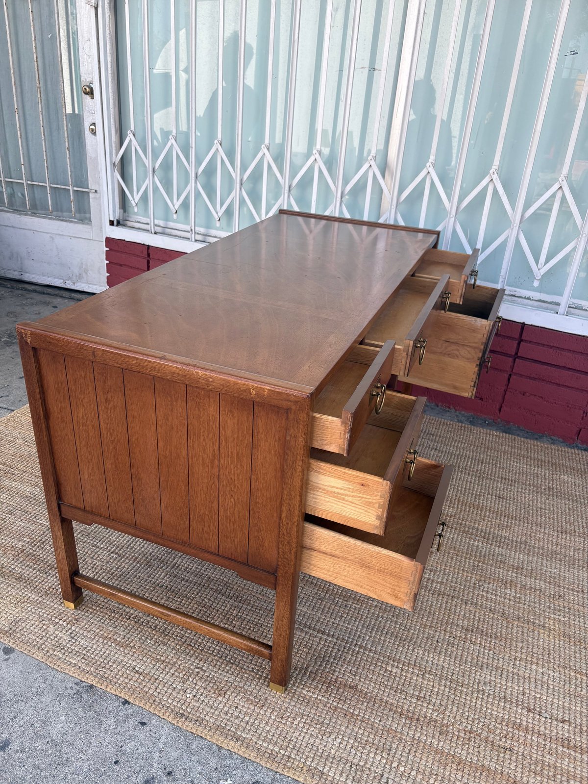 Wooden desk with multiple open drawers displayed outdoors against a corrugated metal backdrop