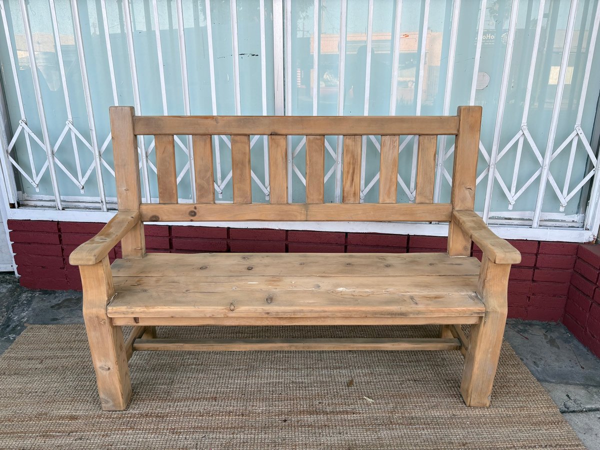 Wooden garden bench with a slatted backrest, positioned in front of white conservatory doors and red planters.