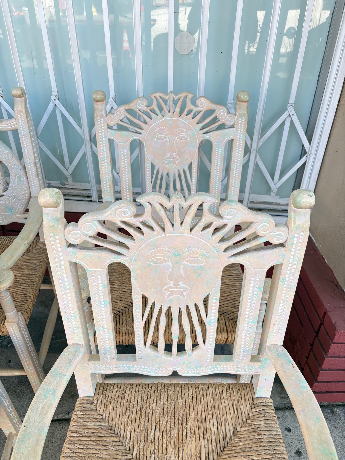Pair of decorative white wicker chairs with ornate sun face carvings on seat backs