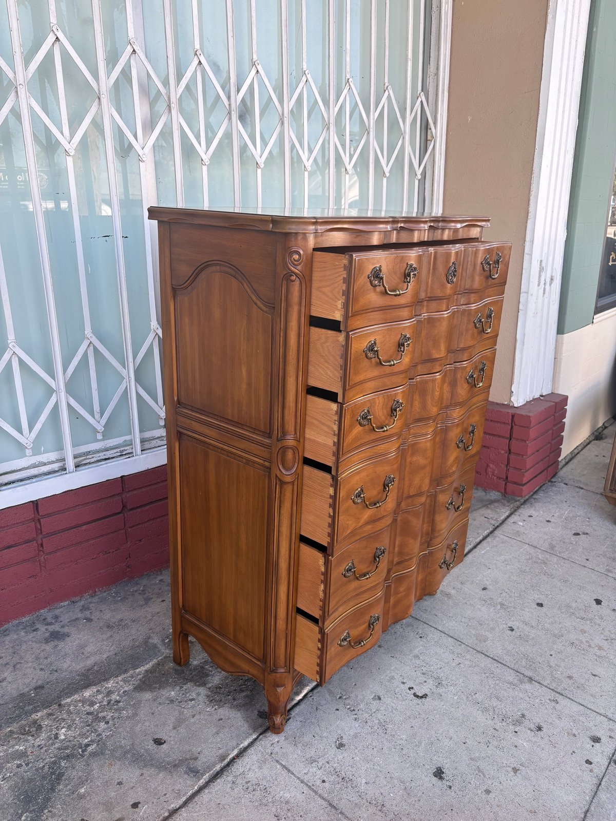 Antique wooden dresser with multiple drawers and ornate hardware on a sidewalk in front of a building