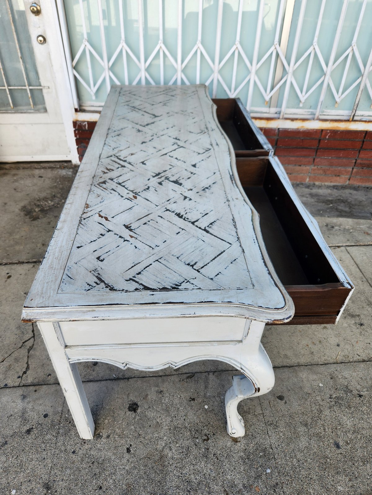 Vintage white console table with blueprint pattern top and open wooden drawer on concrete patio