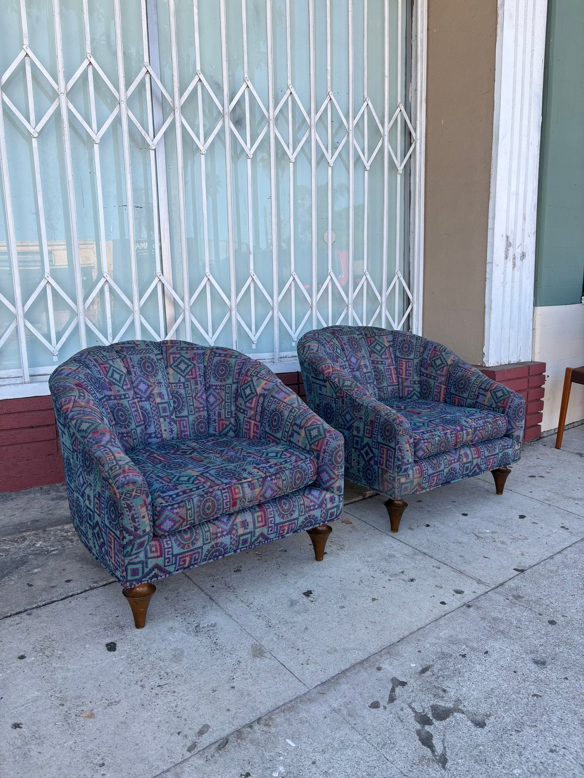Two patterned upholstered armchairs on a concrete sidewalk in front of metal security gate