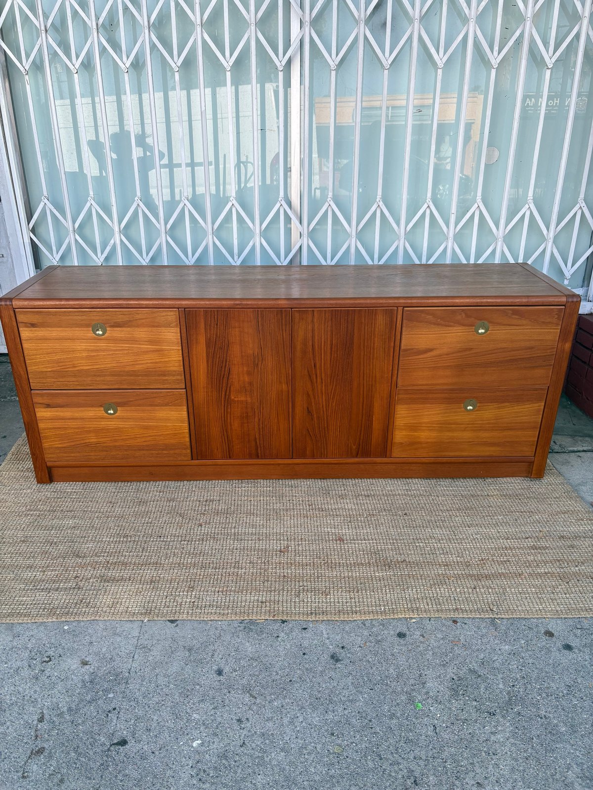 Mid-century wooden sideboard with drawers and central sliding door cabinet against white security gate background