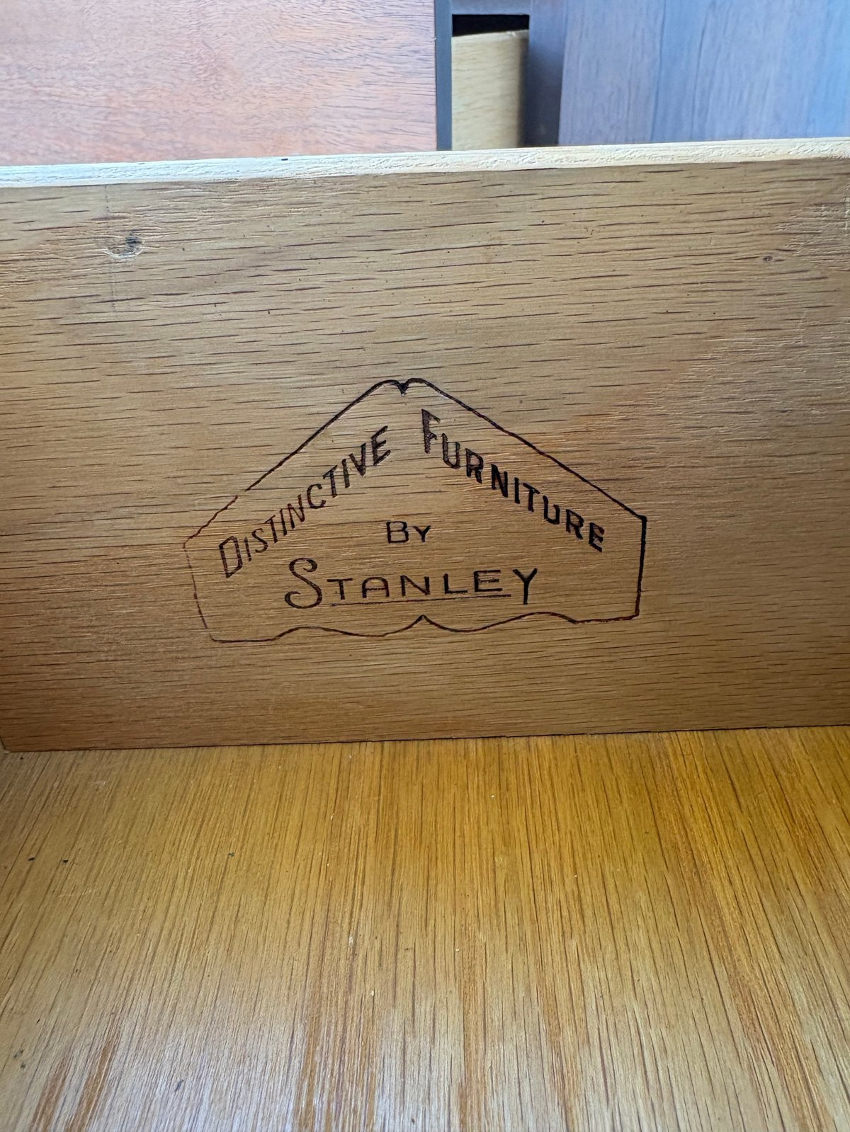 Close-up of a wooden furniture piece showing an engraved Distinctive Furniture by Stanley makers mark on its surface