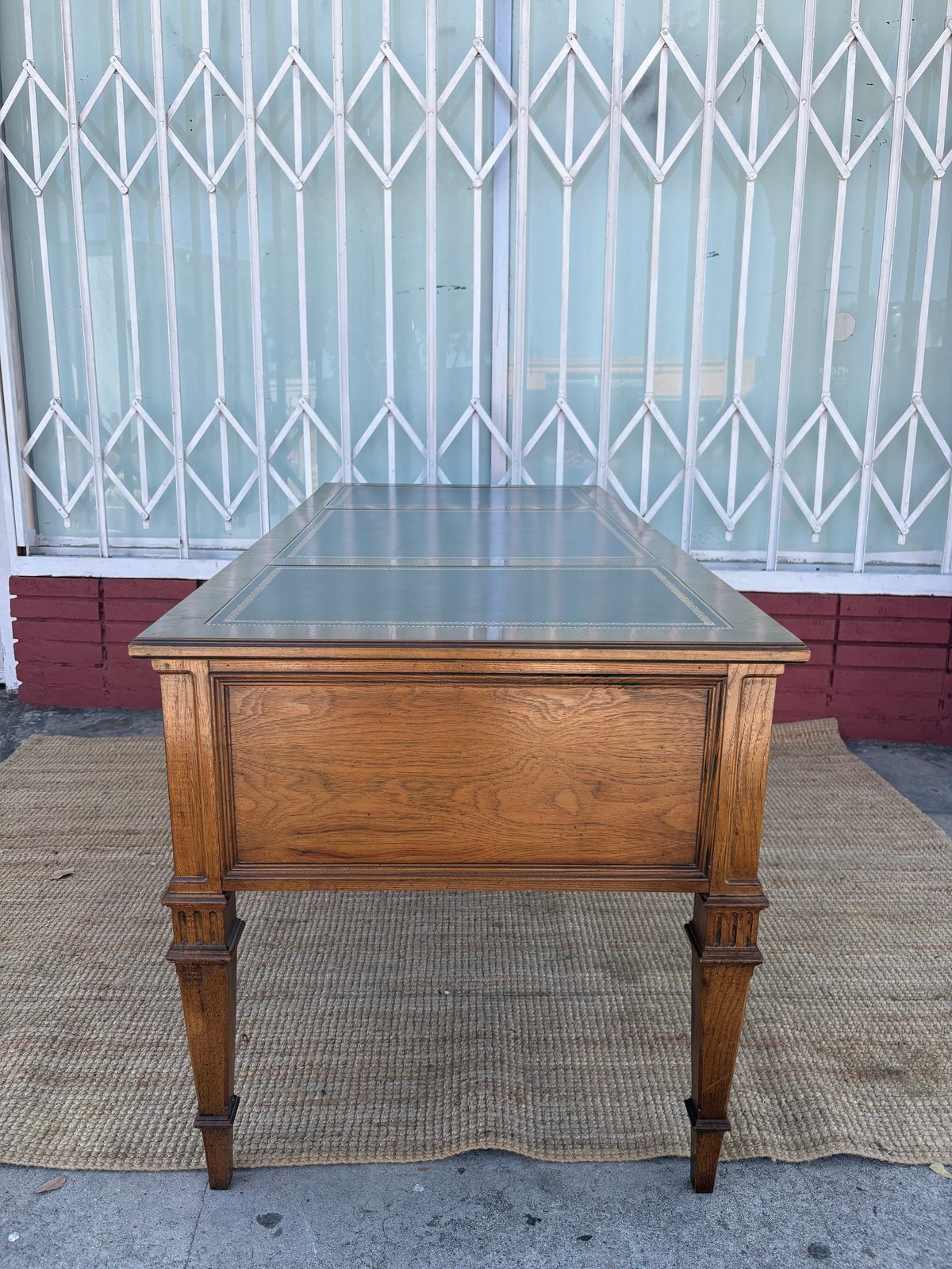 Vintage wooden desk with dark glass top and turned legs on a concrete surface against a white accordion gate