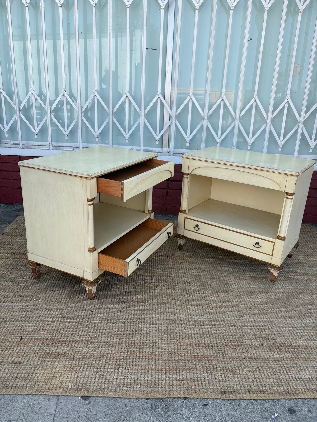 Two cream-colored vintage nightstands with wooden drawers displayed against a corrugated metal backdrop