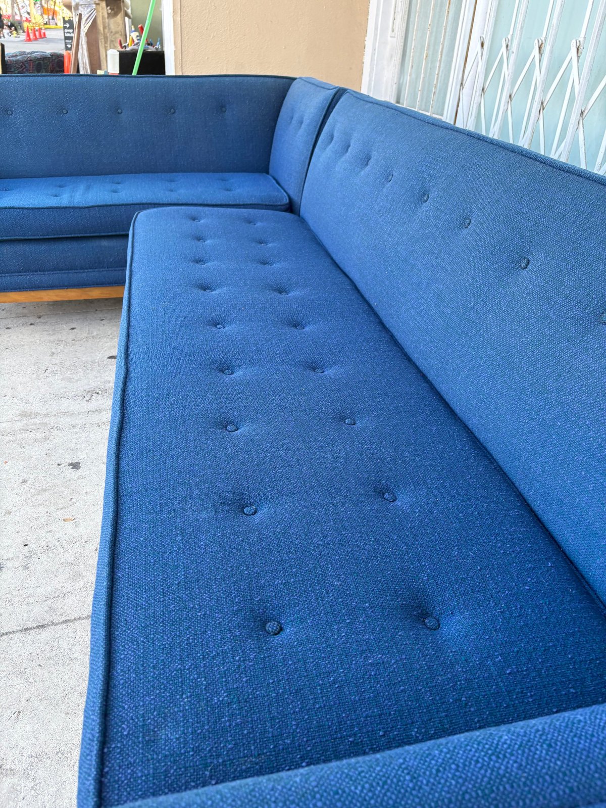 Blue tufted sectional sofa with wooden legs displayed in a showroom