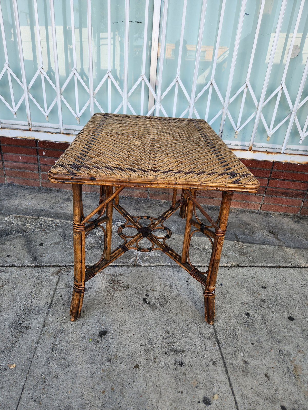 Wicker-topped bamboo side table on concrete with white metal gate in background