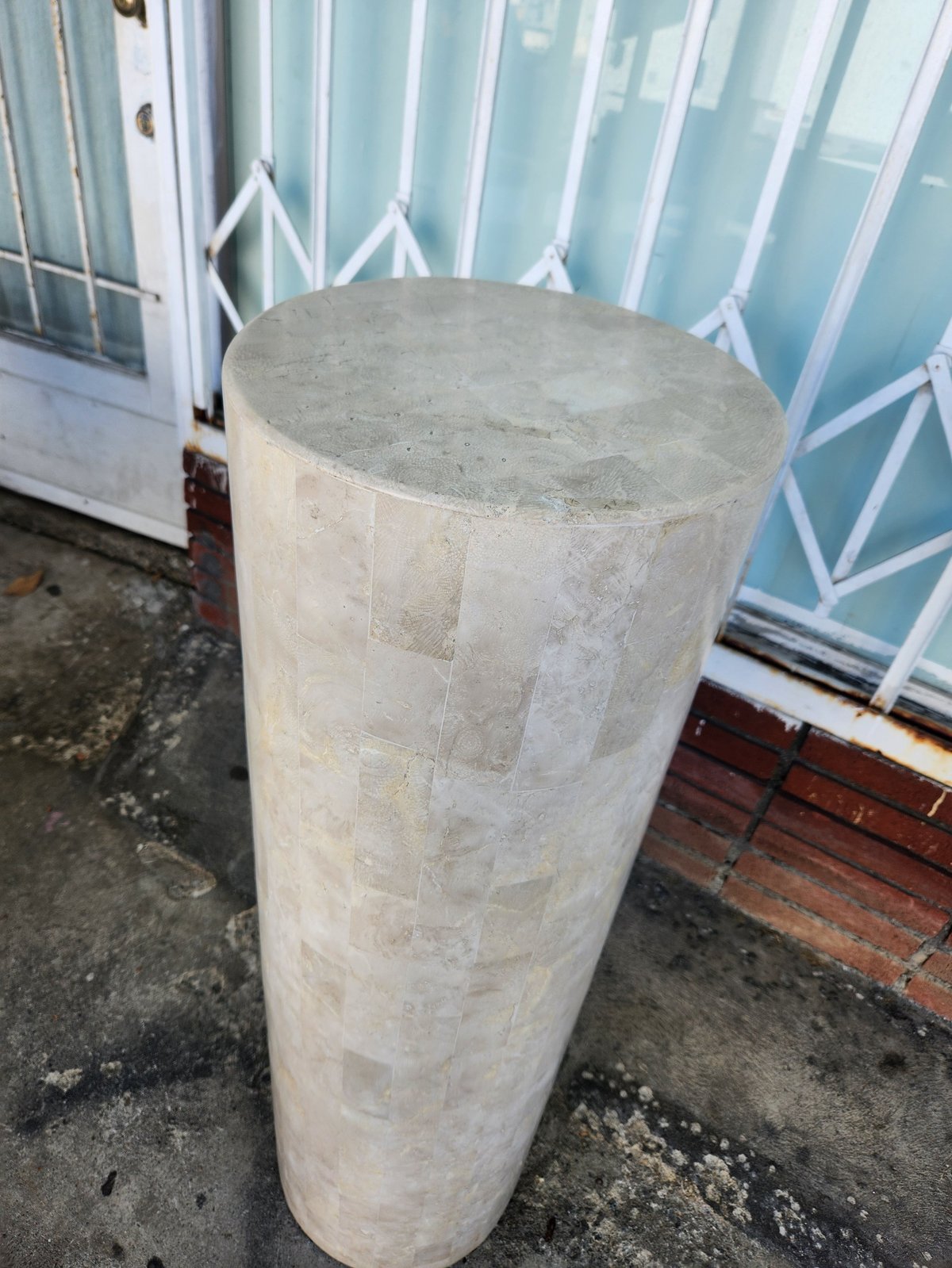 Tall cylindrical concrete post or pillar standing on a patio next to a glass door and white railing
