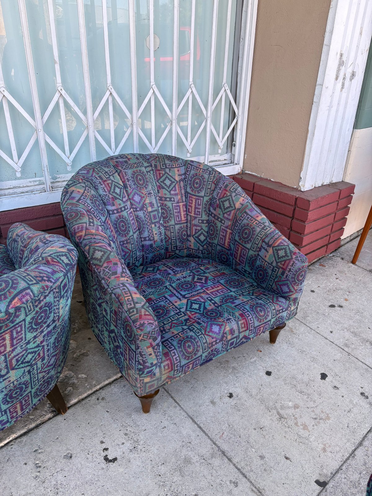 Upholstered armchair with colorful geometric pattern fabric on an outdoor patio next to shuttered window