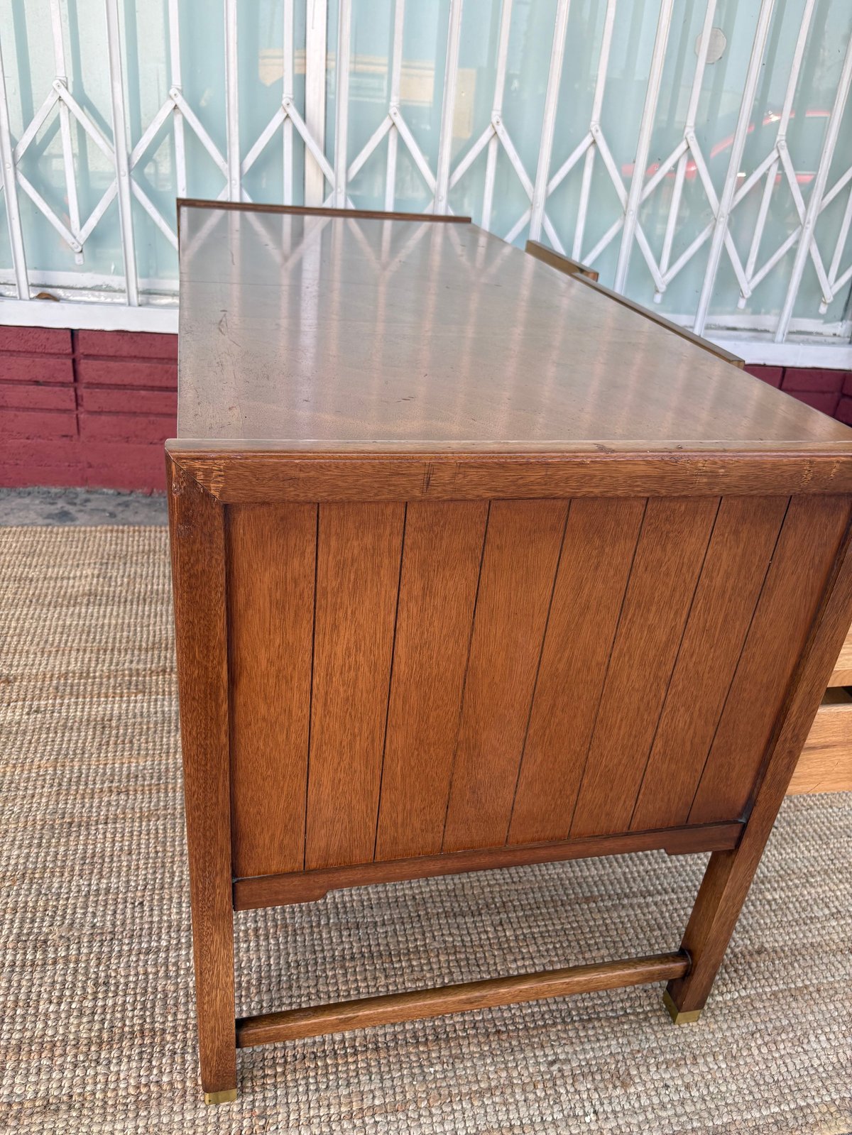 Wooden desk with glass top and vertical slat panels, displayed against a window and red brick building