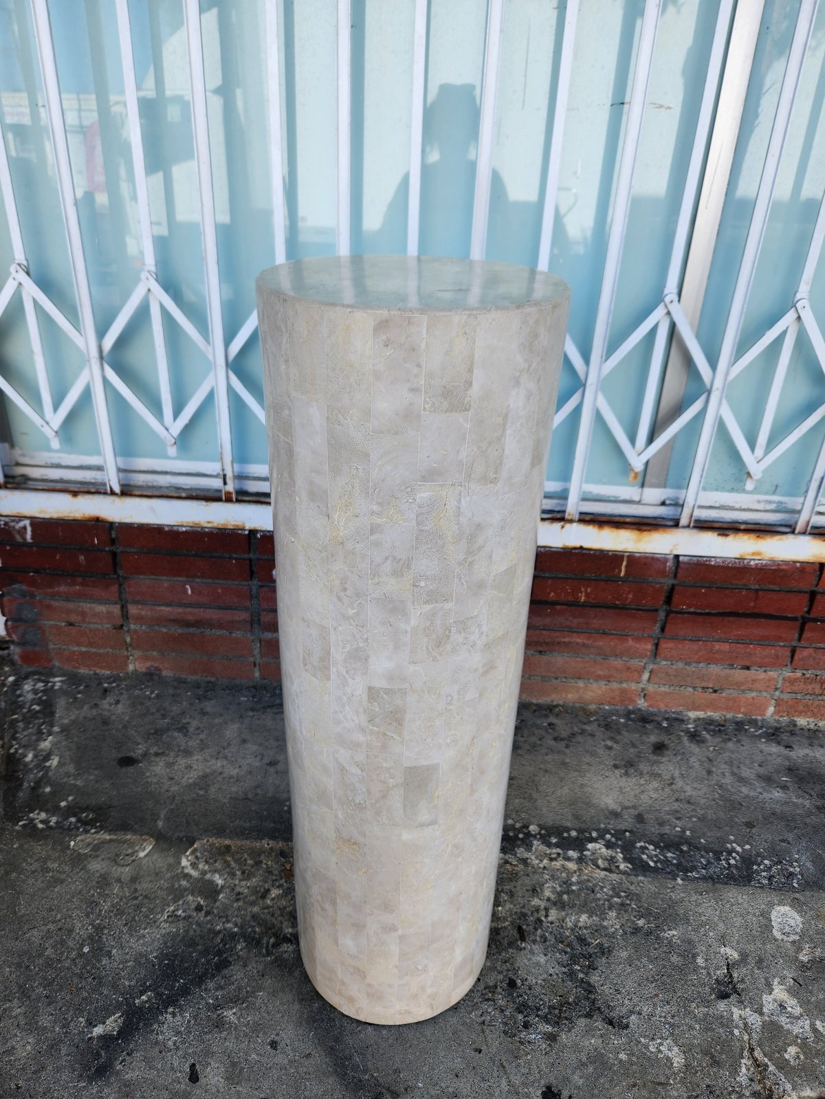 Tall cylindrical concrete column or post standing on a dark floor against a window with white latticed curtains