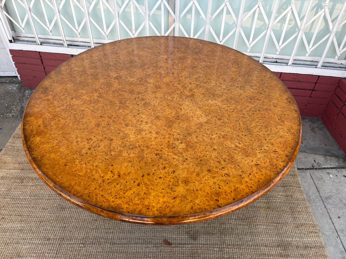 Large round wooden table with honey-brown finish displayed on pavement outdoors