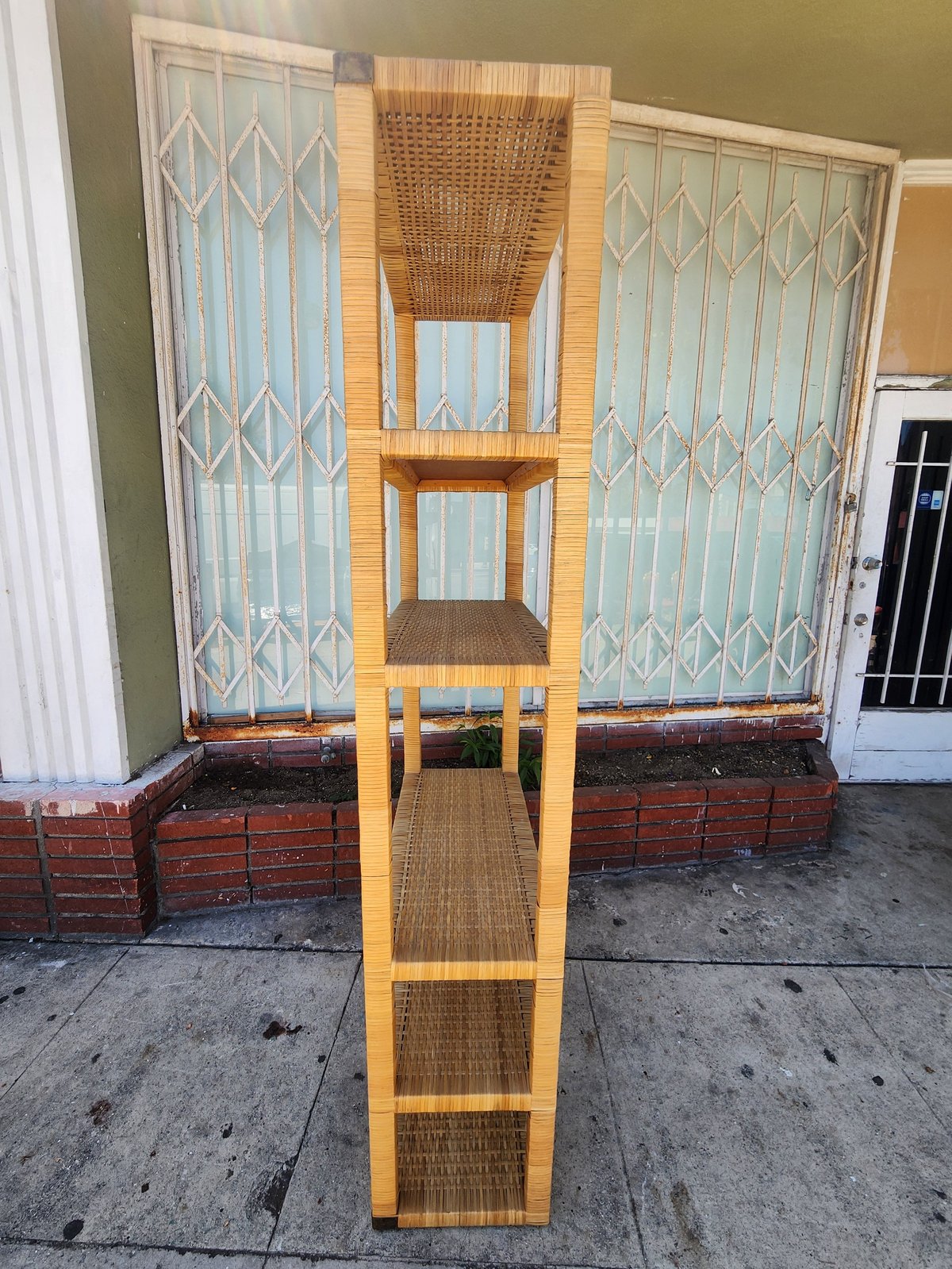 Tall wooden shelving unit with woven wicker backing displayed on a sidewalk in front of a building