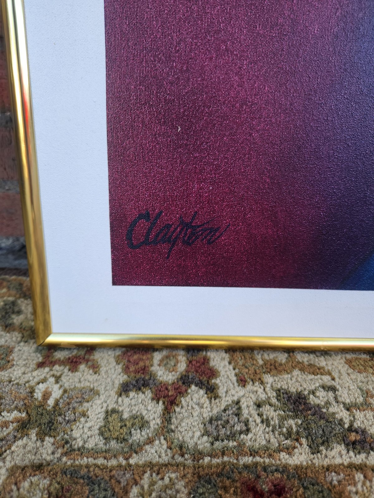 Framed art print with burgundy gradient background and artist signature, displayed on patterned carpet