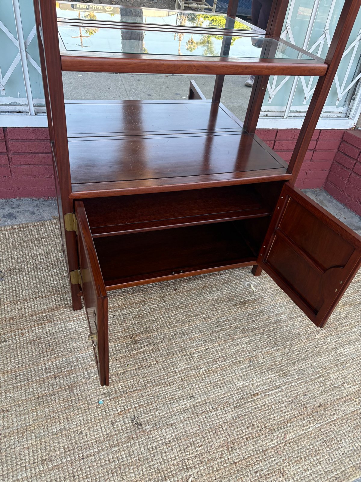 Dark wood display cabinet with glass top doors and open wooden cabinet door below, displayed in a storefront window