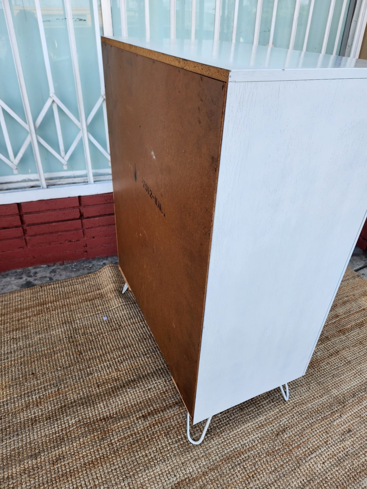 A folding room divider with a brown wood panel on one side and white panel on the other, standing in an entryway near a metal gate