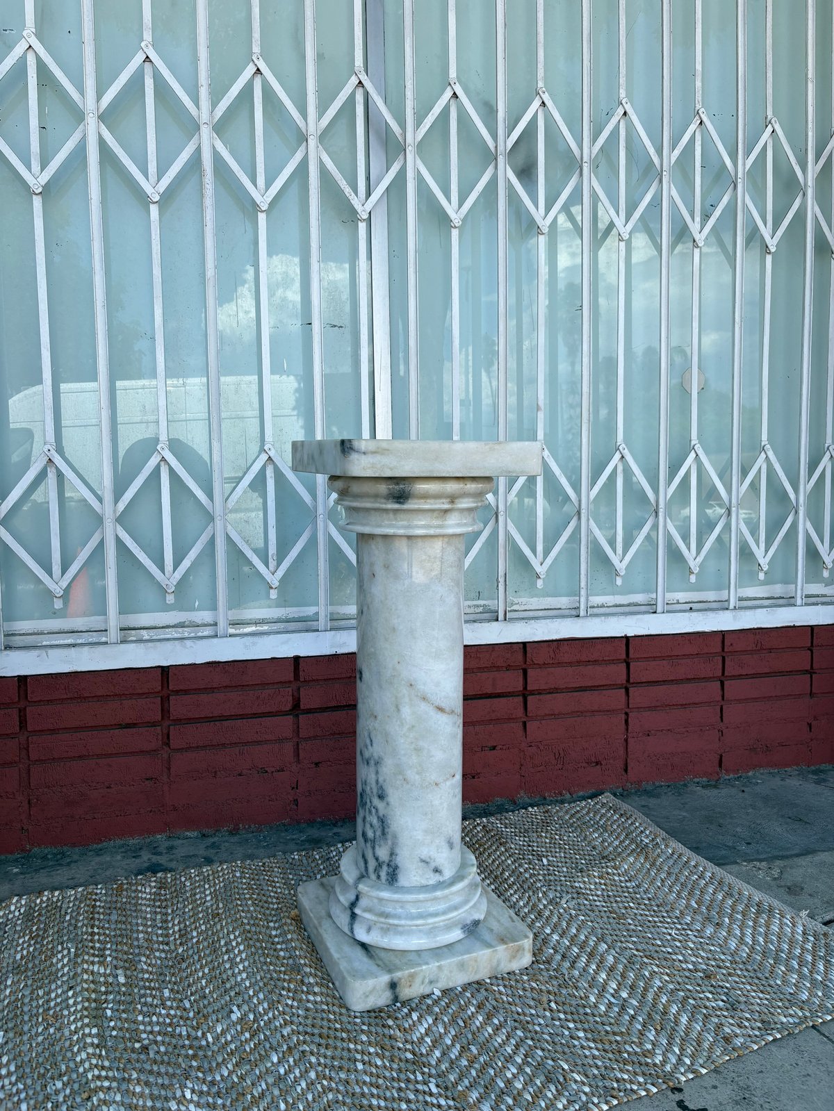 Weathered concrete column with capital on brick and metal accordion gate background