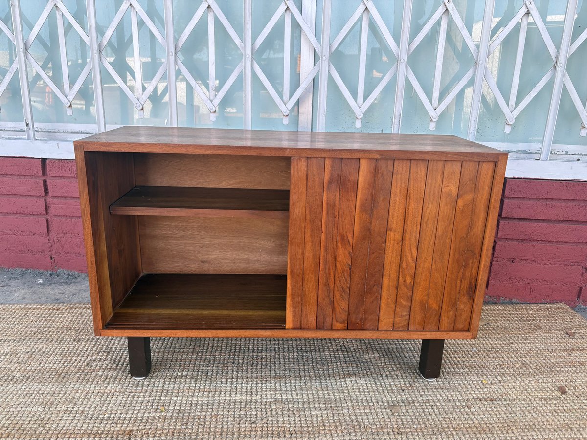 Mid-century wooden sideboard with open shelving on left and vertical slat cabinet doors on right, featuring dark legs and warm wood finish