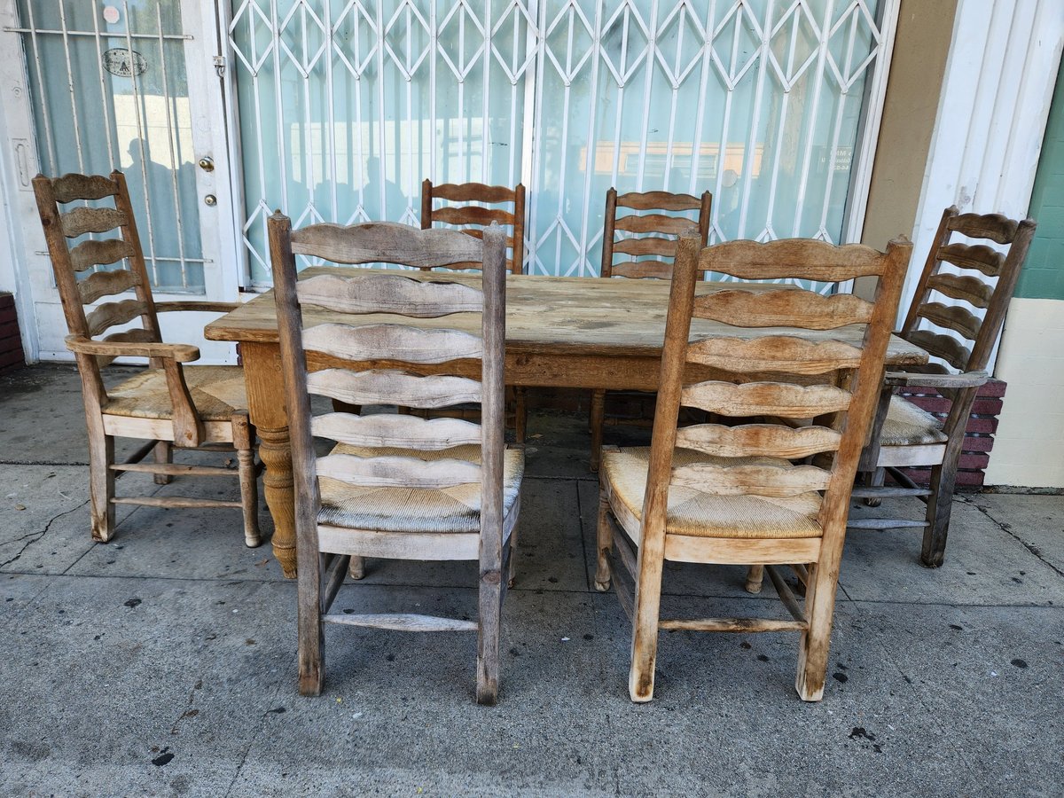 Wooden dining table with six rush-seat ladder-back chairs arranged in a room with large windows