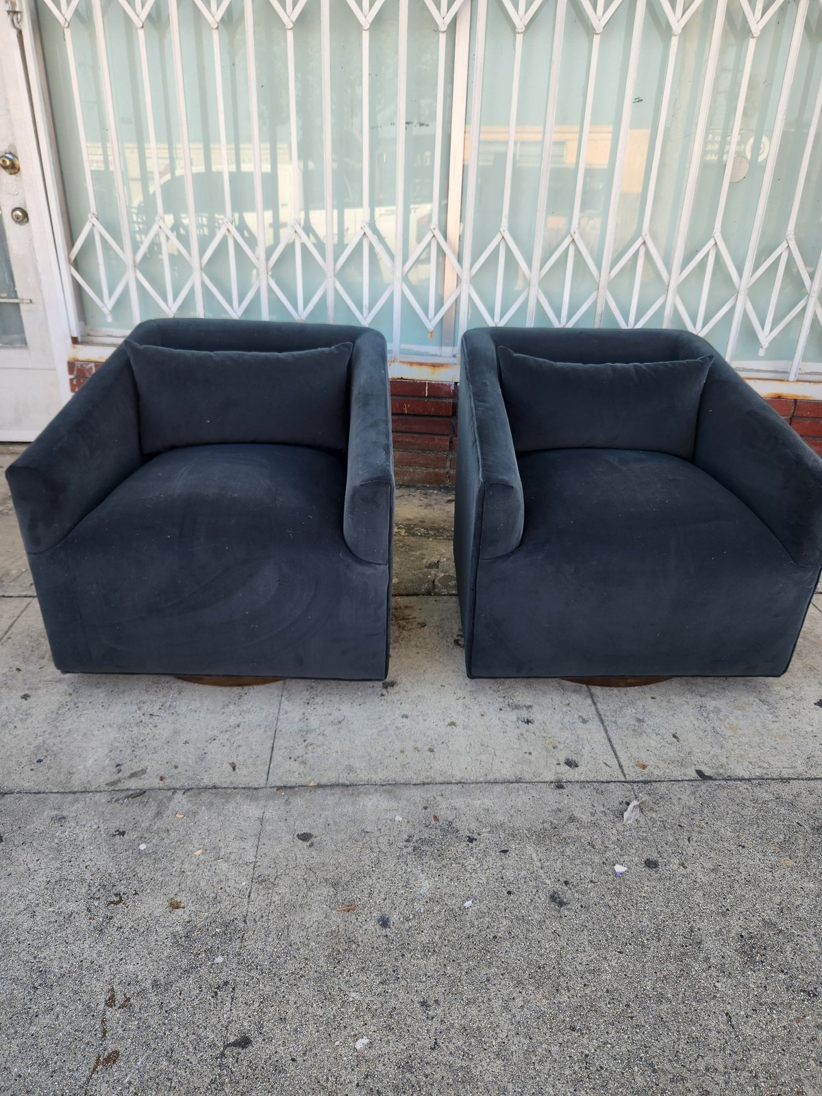 Two dark blue upholstered cube armchairs sitting on concrete outside a storefront with metal security gates