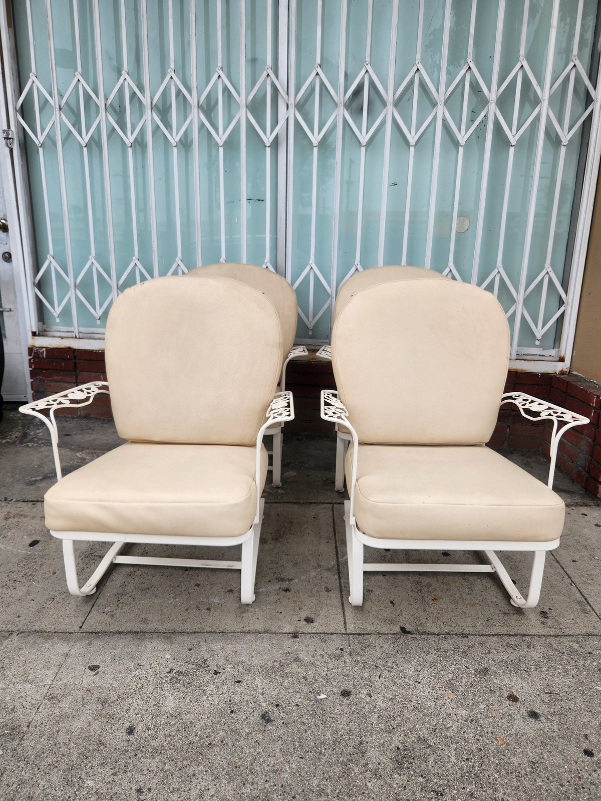 Two cream-colored metal outdoor chairs with cushions on a driveway in front of a blue corrugated metal garage door