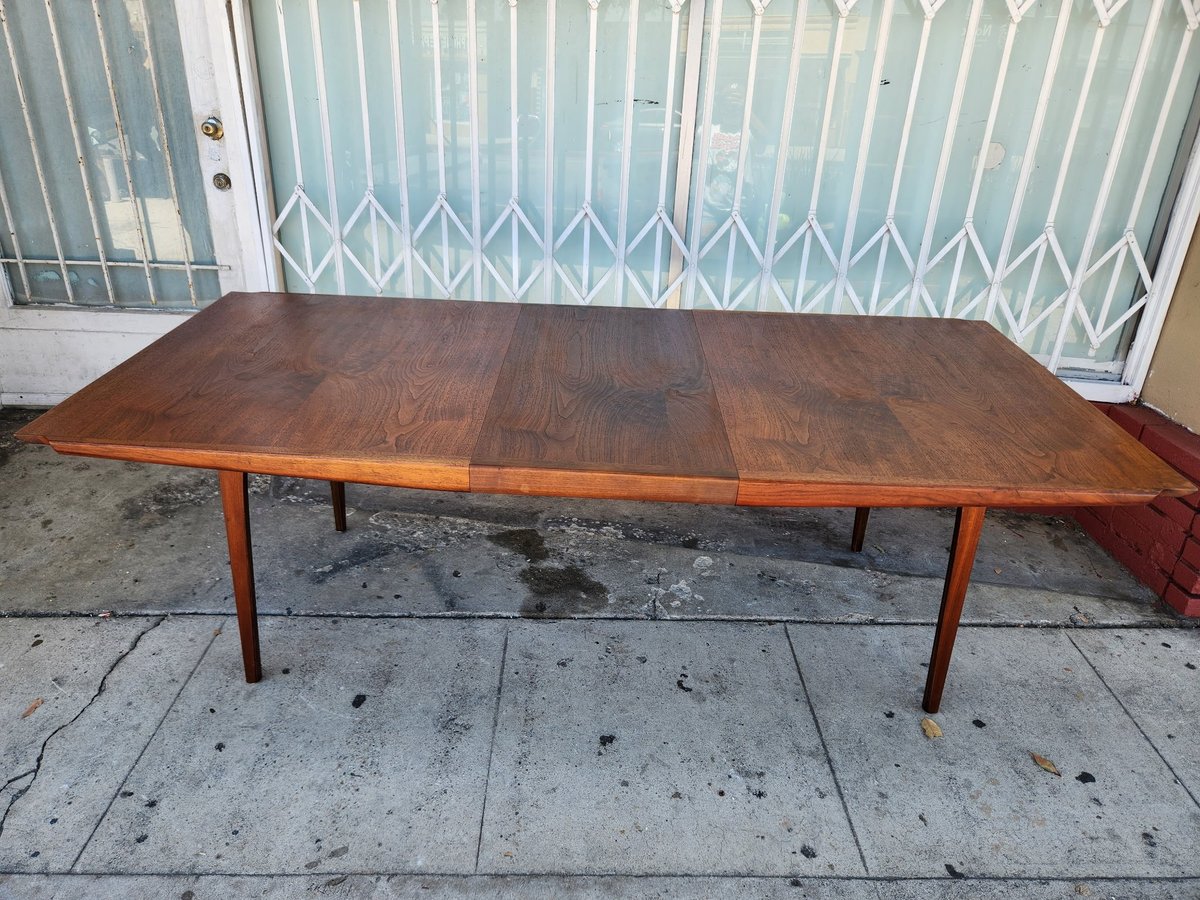 Mid-century modern wooden dining table with tapered legs on concrete ground in front of metal security gate