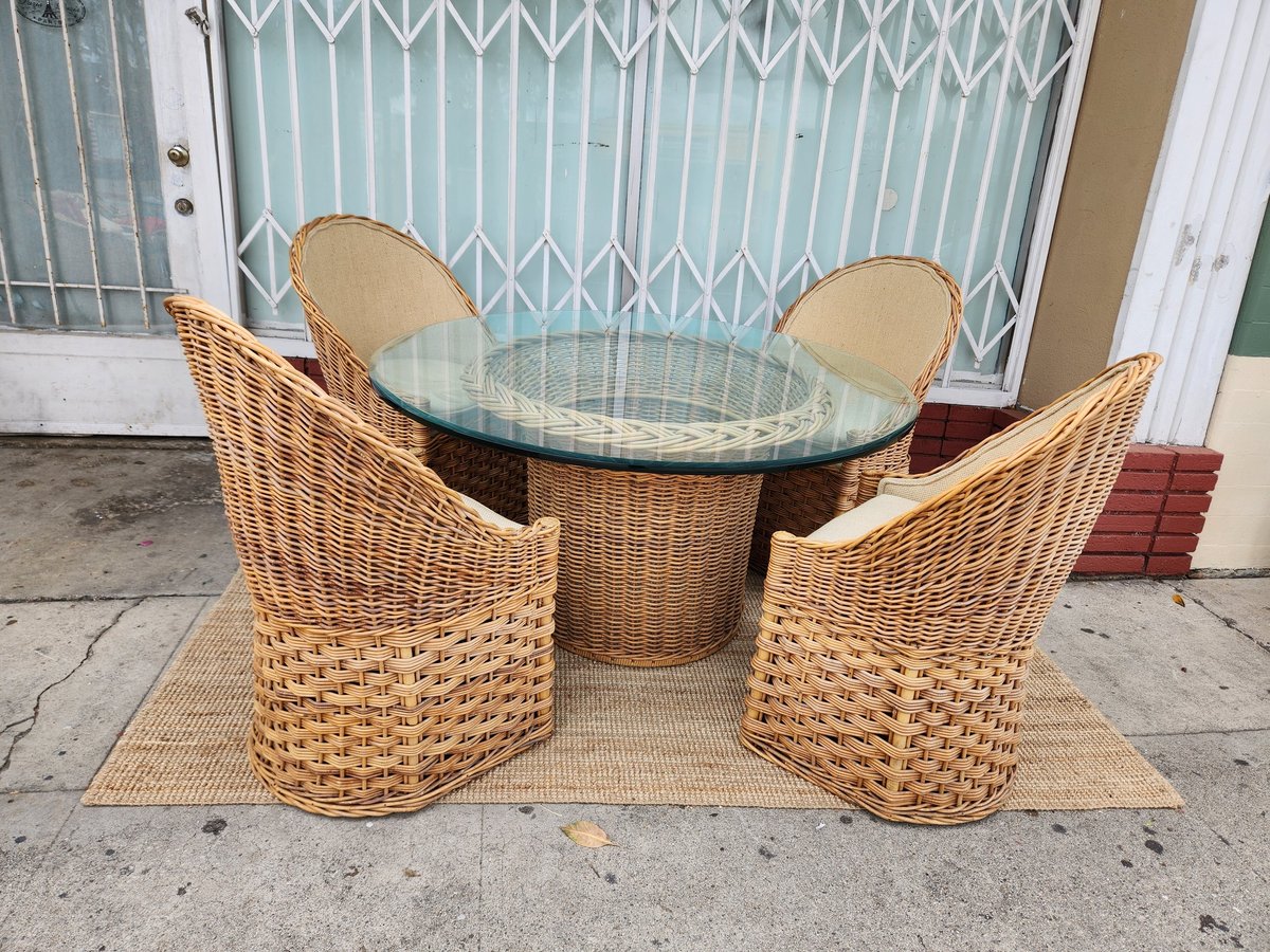 Wicker patio dining set with two curved chairs and round glass-top table on concrete patio