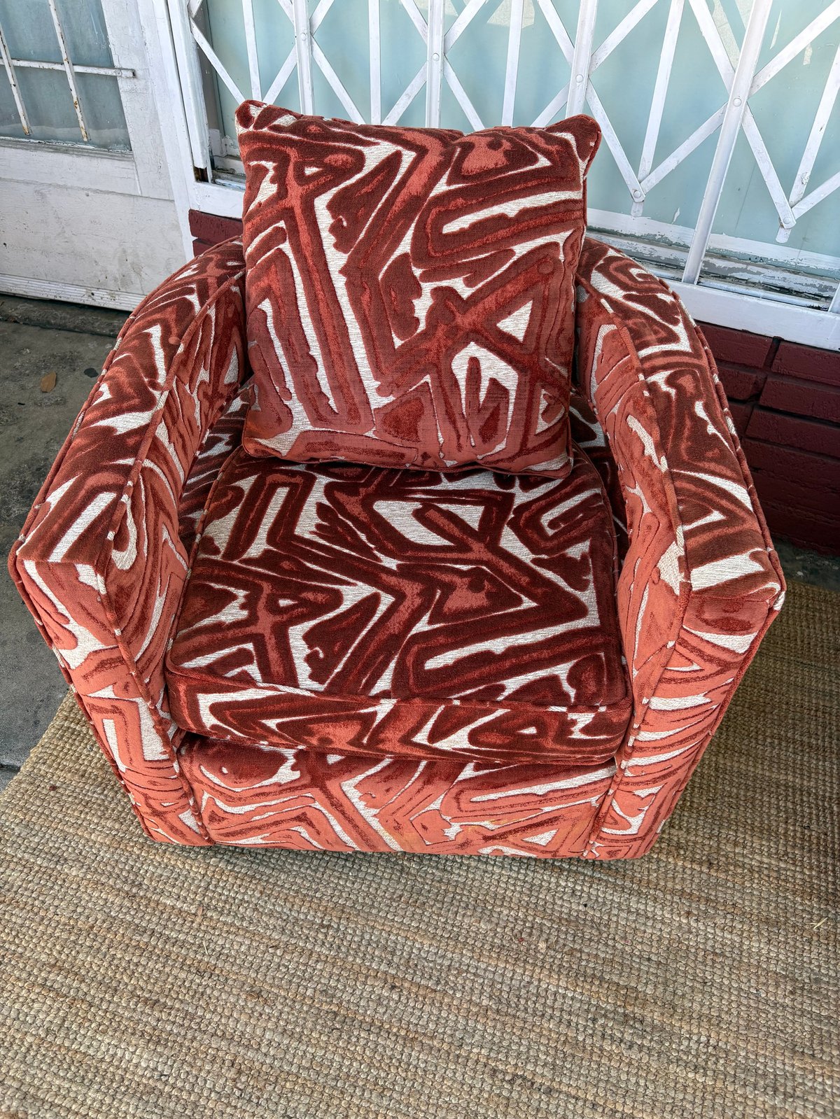 Red and white patterned upholstered armchair with decorative pillow on carpeted floor near glass doors