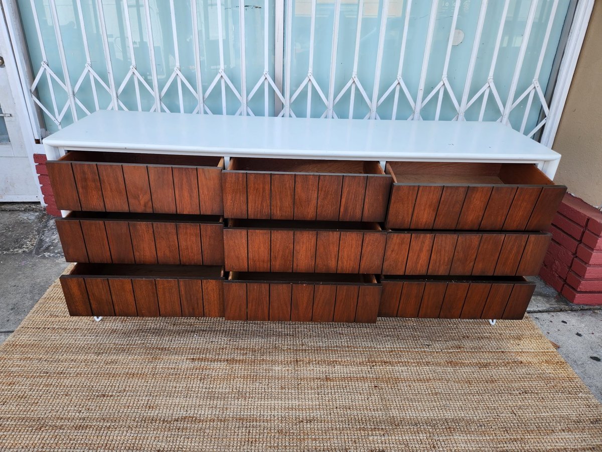 Wooden dresser with three drawers stacked on a textured doormat in front of a white accordion gate