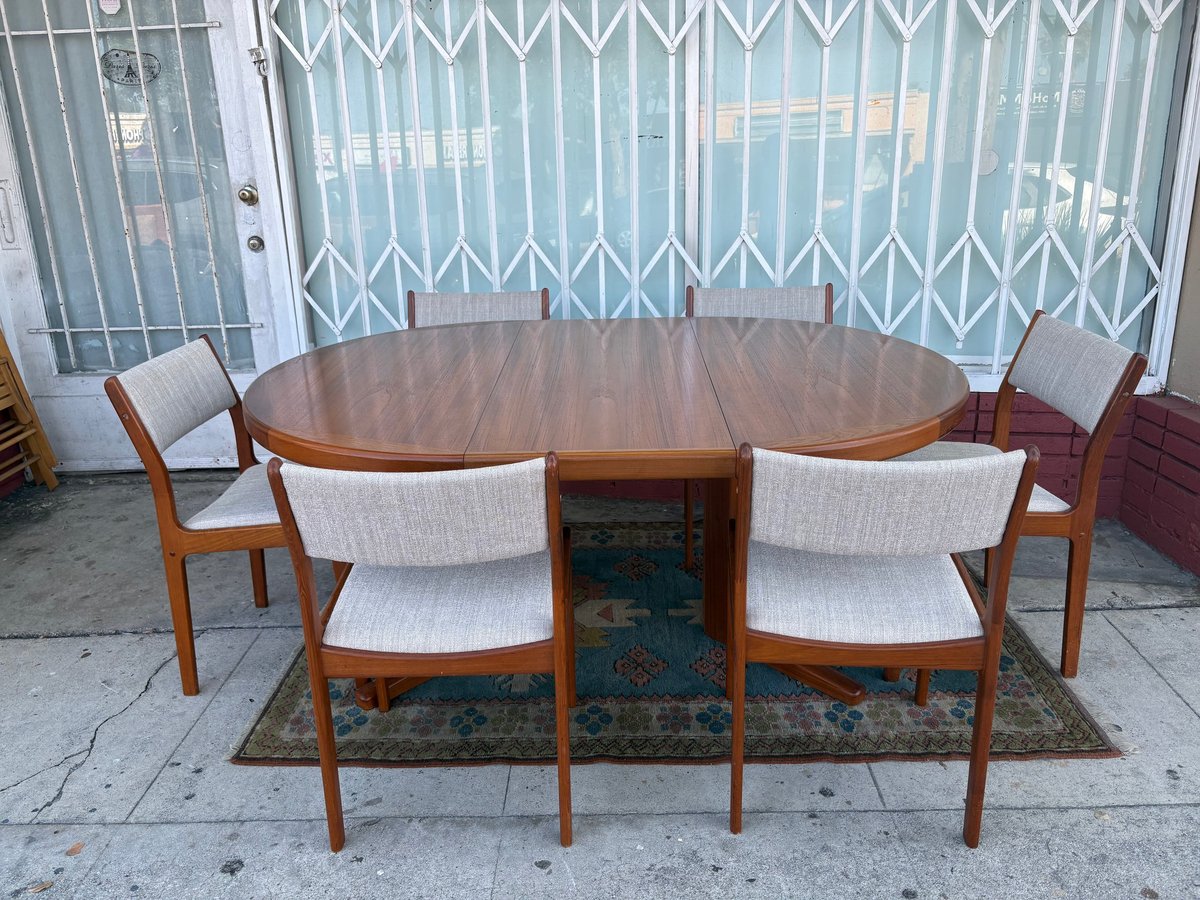 Mid-century modern dining set with oval wooden table and four upholstered chairs on a patterned rug, in front of metal accordion doors