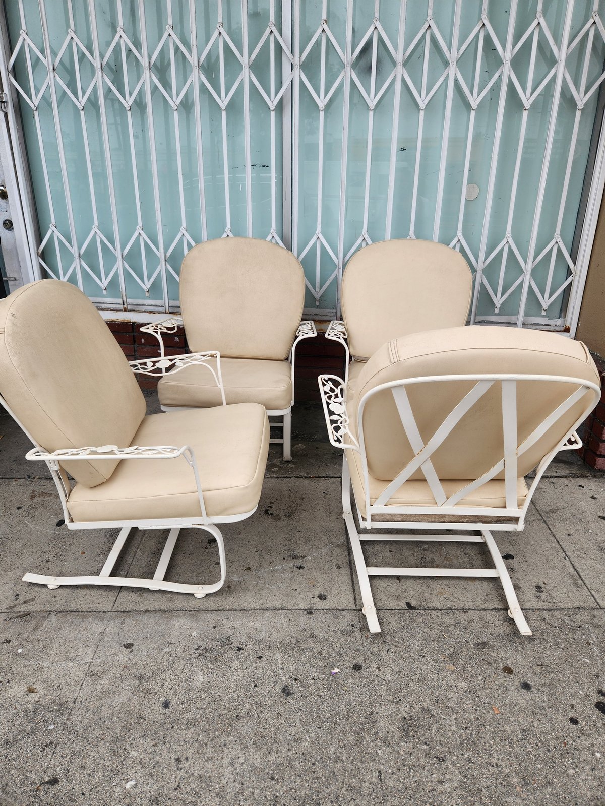 Set of four cream-colored patio chairs with white metal frames arranged in front of a teal accordion door