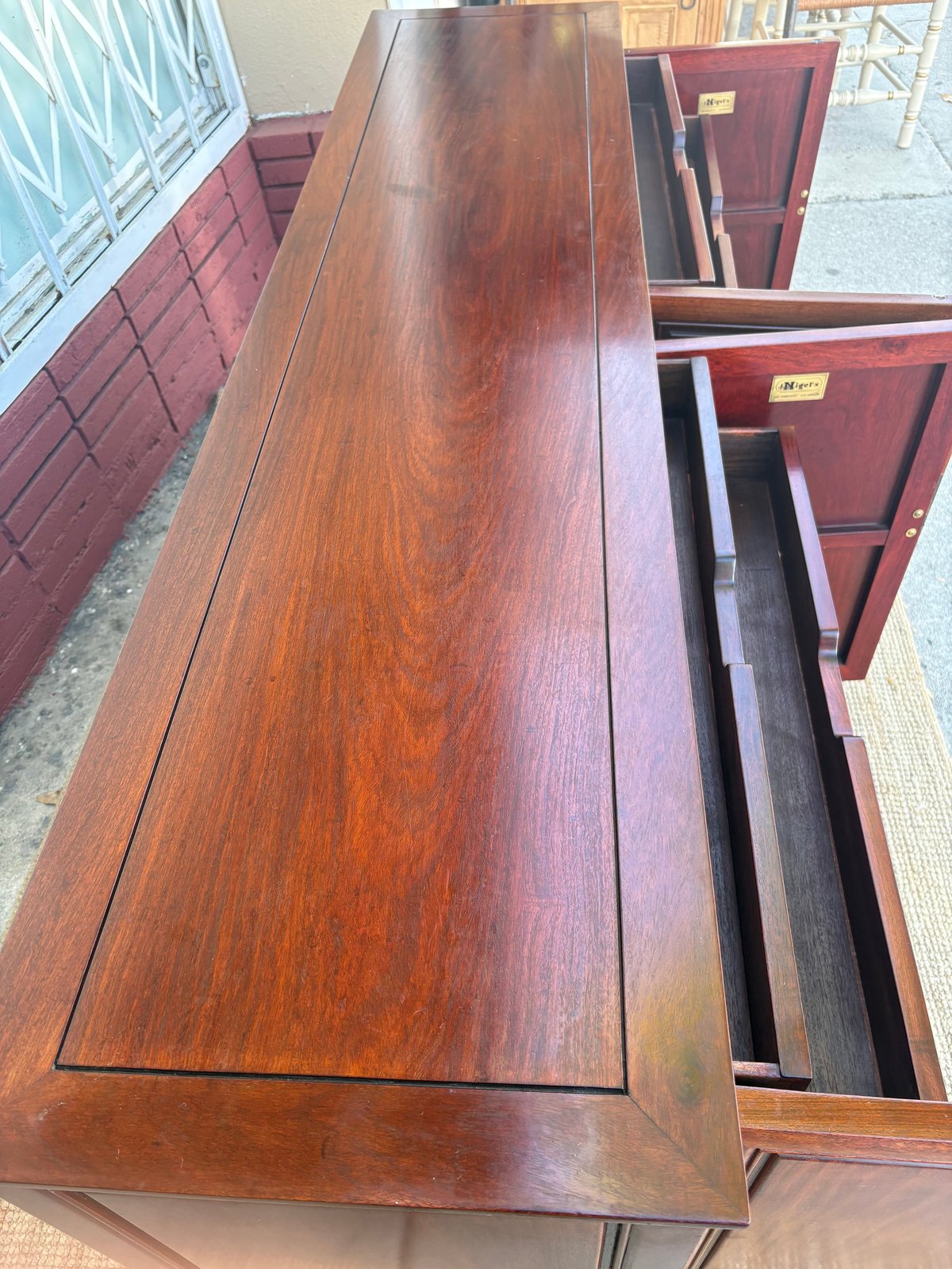Large wooden table with deep grain finish, one drawer open, and burgundy wooden chairs visible in background