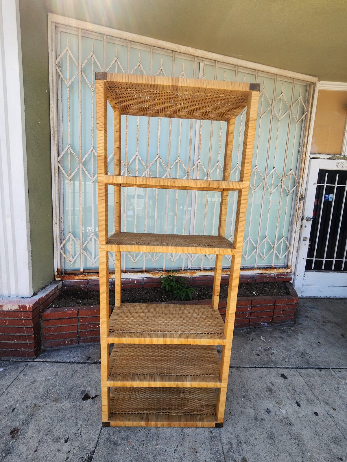 Vintage wooden shelving unit with woven rattan shelves standing on a concrete patio outside a home