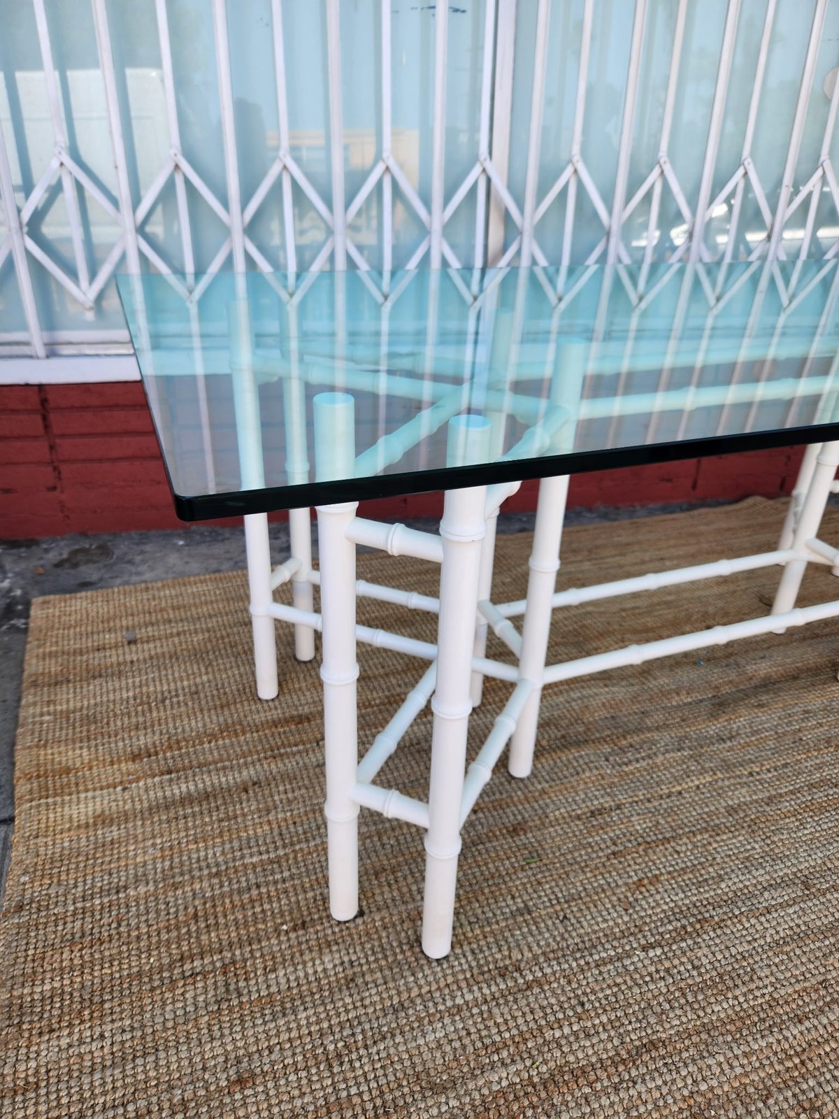 Glass-top table with white wooden legs and beige diamond patterned curtains in background on tan carpet