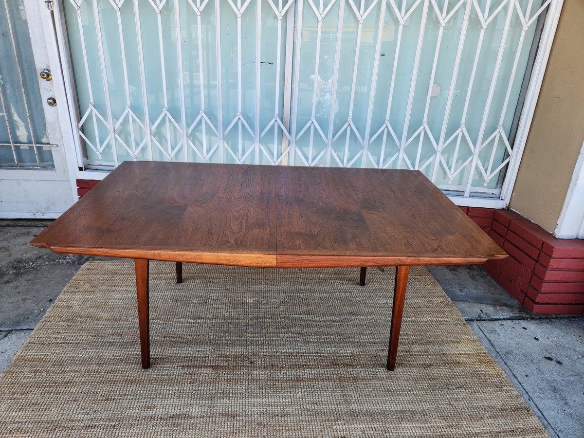Mid-century modern wooden dining table with four legs on a beige area rug in a home entryway