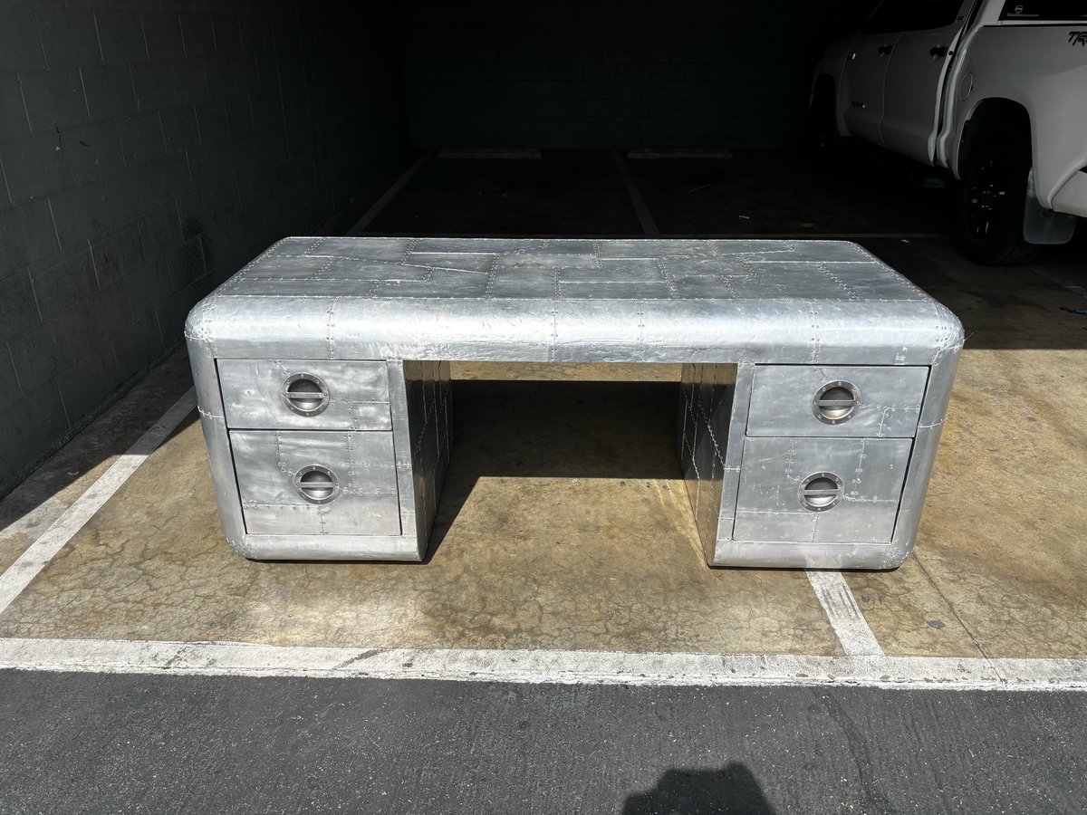 Vintage gray metal desk with drawers, featuring a central open compartment, positioned on a concrete floor in a garage setting.